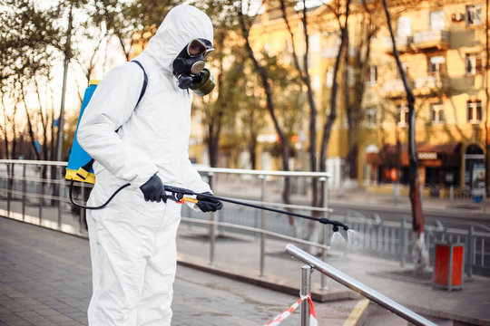 Man wearing personal protective equipment suit, gloves and gas mask cleaning the streets protected with warning tape with a backpack of spray disinfectant water to remove covid-19 coronavirus.