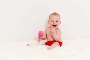 Fototapeta na wymiar eight-month-old cute Caucasian baby girl in red panties sits on the bed and laughs.