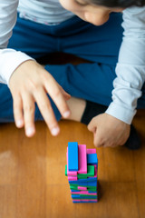 Close up of boy playing colorful wooden blocks stack tower game for kids on house floor spending entertaining time at home