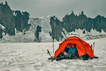A guy and a girl in a red tent on a large glacier. Huge rock wall.