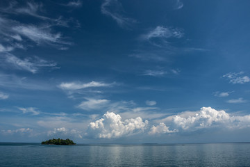 Little green island in the ocean. Big white clouds on the horizon