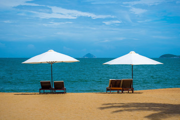 Two white umbrellas and deck chairs on a beautiful empty sunny beach. Calm ocean and islands on the horizon. Vietnam, Nha Trang