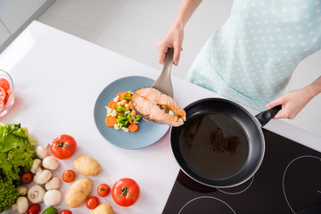 High angle view cropped photo of housewife lady put grilled salmon fillet steak flying pan ready roasted on plate with garnish cooking dinner wear apron t-shirt stand modern kitchen indoors