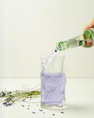 Someone is pouring lavender lemonade from bottle in highball glass, closeup view
