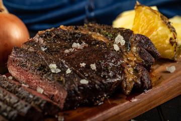 Sliced meat rib eye steak served with pineapple on a wooden board, sea salt on it