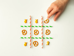 Hand playing tic-tac-toe game with small dry crackers and paper drinking straws, flat layout