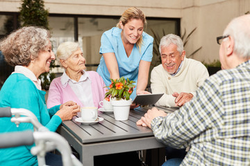 Pflegekraft mit Tablet und eine Gruppe Senioren