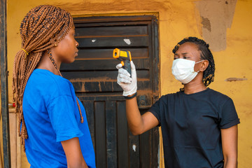 young black lady using a handheld infrared thermometer to test a lady's temperature
