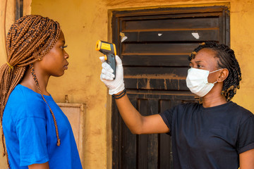 young black lady using a handheld infrared thermometer to test a lady's temperature