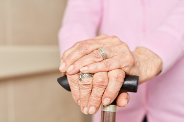 Faltige Hände einer Seniorin mit Gehstock