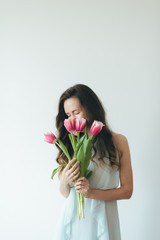 Girl sniffs pink tulips. Beautiful girl hugging bouquet of pink tulips. Woman and tulips