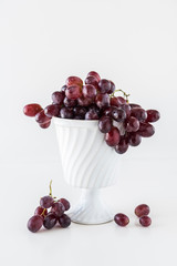 Juicy dark red grapes in an old white bowl on a white table