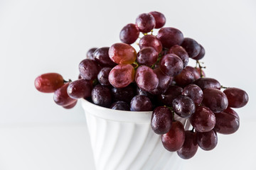 Closeup of juicy dark red grapes in an old white bowl on white background