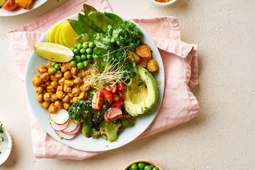 Healthy vegetarian lunch bowl with avocado, chickpeas, quinoa and vegetables, garnished with microgreens and nut dressing. Flat lay on stone background.