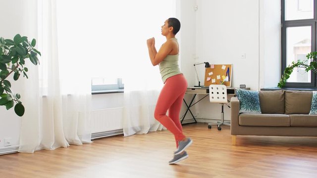 sport, fitness and healthy lifestyle concept - african american woman running on spot at home