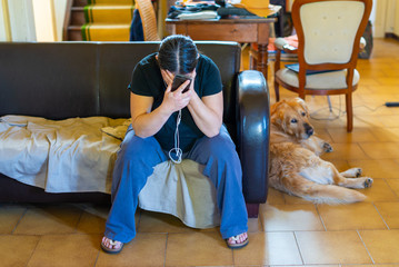 woman at home sitting on sofa with hands on head and smartphone, very sad and lonely, dog near her