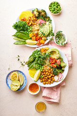 Healthy vegetarian lunch bowl with avocado, chickpeas, quinoa and vegetables, garnished with microgreens and nut dressing. Flat lay on stone background.