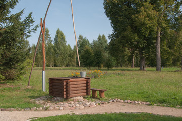 Old village well-crane with bucket for water in the field among the trees. Forest and blue sky.