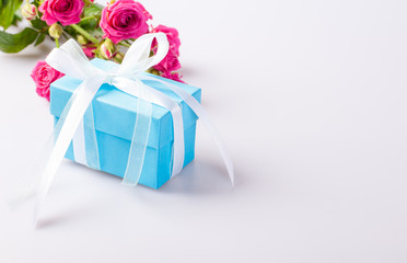 Blue gift box with white ribbon bow and bouquet of red roses on white background