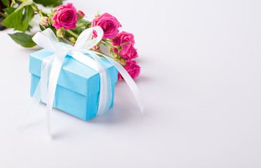 Blue gift box with white ribbon bow and bouquet of red roses on white background