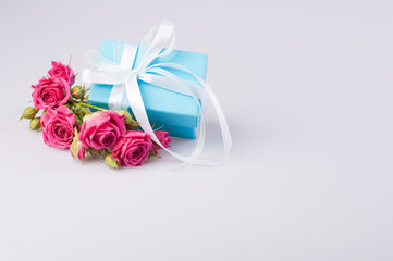 Blue gift box with white ribbon bow and bouquet of red roses on white background