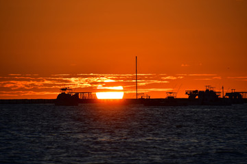Orange sun rising from the horizon at dawn against the background of silhouettes of fishing boats