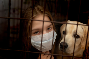 Young woman in mask behind girds or bars with her dog. forced home isolation