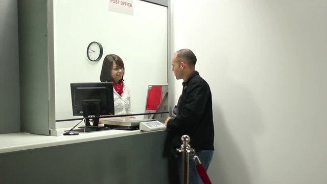 Man talking at the Post Office Counter - The Female assistant helps the man - Stock Video Clip Footage - Tracking Shot
