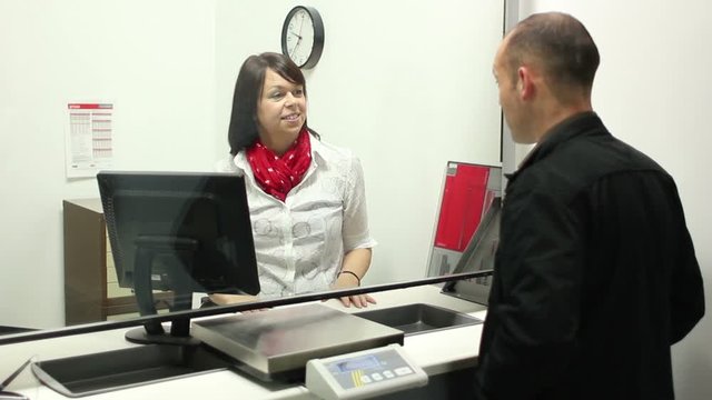 Caucasian Man buying Stamps at the Post Office Counter - The Female assistant serves the man - Stock Video Clip Footage - Tracking Shot
