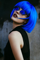 Woman with short electric blue hair and sunglasses posing on urban wall background. Concept of future and cosmos. 