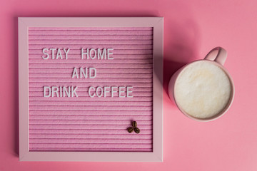 Top view of Pink Coffee cup with cappuccino and qoute Stay home and drink coffee. Self isolation and quarantine campaign to protect yourself from pandemia.