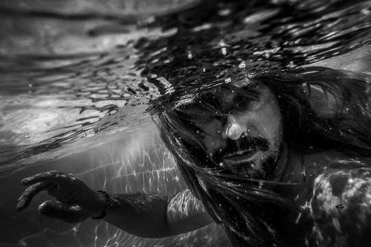 Artistic pic out of focus underwater with long hair man swimming with bubble in water, dark underwater atmosphere with nightmare human abyssal creature like mermaid with beard