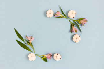 Square frame made of alstroemeria flowers, cotton and green leaves on a blue pastel background. Holiday floral composition.