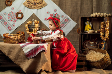 Little girl wearing red headband and ornamental shirt pouring tea from samovar celebrating Maslenitsa