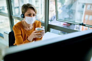 Thoughtful female entrepreneur wearing face mask while using computer in the office.