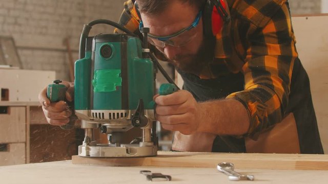 Carpentry industry indoors - man worker in protective glasses and headphones grinding a wooden item in the workshop