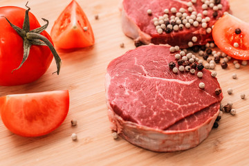 raw meat lies on a board with black pepper and tomatoes