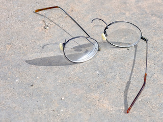 A pair of Titanium Wire Rim eye glasses that have broken and split apart on the nose bridge section while laying on a cement surface.