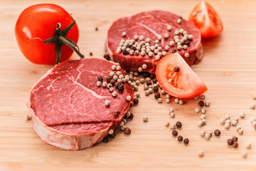 raw meat lies on a board with black pepper and tomatoes