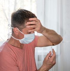 Man in protective face mask holding thermometer at home
