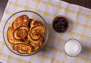 Pancakes on a plate, milk in a glass, and jam on a napkin on the table.