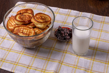 Pancakes on a plate, milk in a glass, and jam on a napkin on the table.