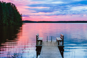 Two wooden chairs bench on a wood pier overlooking a lake at sunset