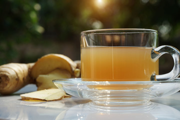 cup of hot ginger tea and gingers root put on wooden table under the morning sun light.