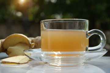 Cup of hot ginger tea and gingers root put on wooden table under the morning sun light.