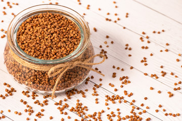 Close-up of buckwheat in a glass jar with a jute cord and scattered on a white wooden table.