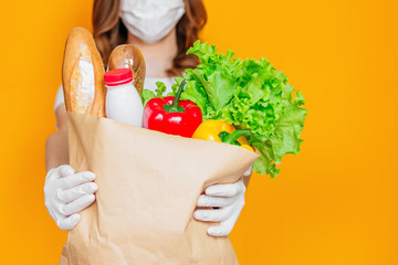 Female hands hold a paper bag with products, vegetables, herbs isolated over orange background, quarantine, coronavirus, safe food delivery, copy space