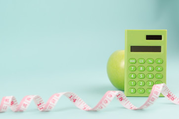Healthy diet concept with a green calculator, measuring tape and apple