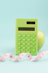 Healthy diet concept with a green calculator, measuring tape and apple