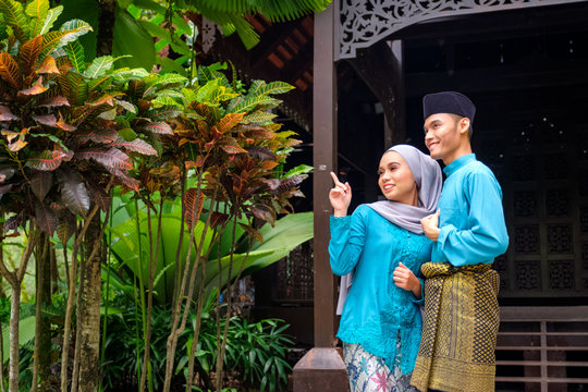 A portrait of young couple of malay muslim in traditional costume during Aidilfitri celebration by traditional wooden house